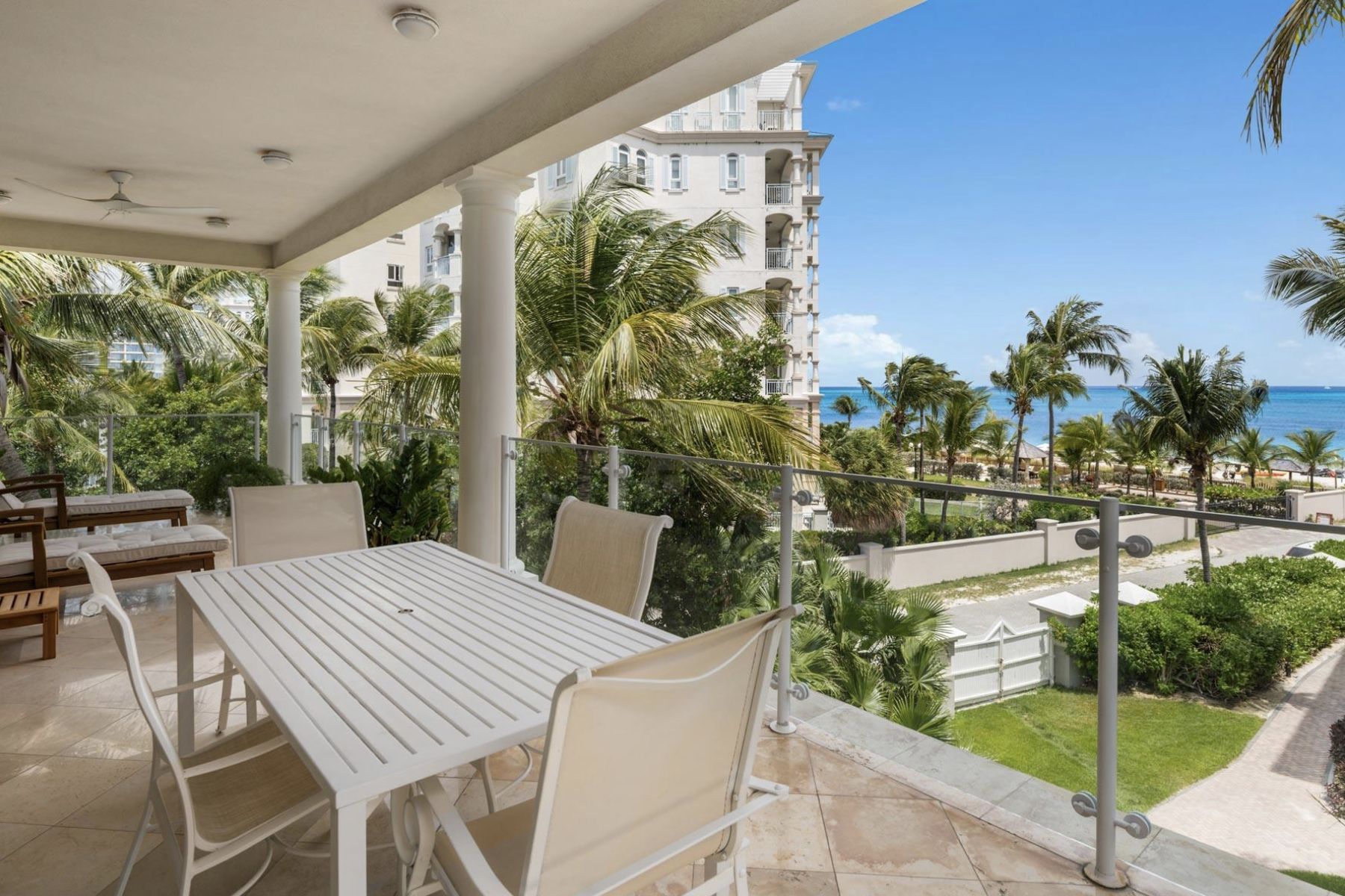 Covered terrace of Residence 308 with dining table, garden and ocean beyond the palms